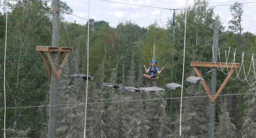 a student floats in a cross-legged position while being suspended in mid-air on a ropes course